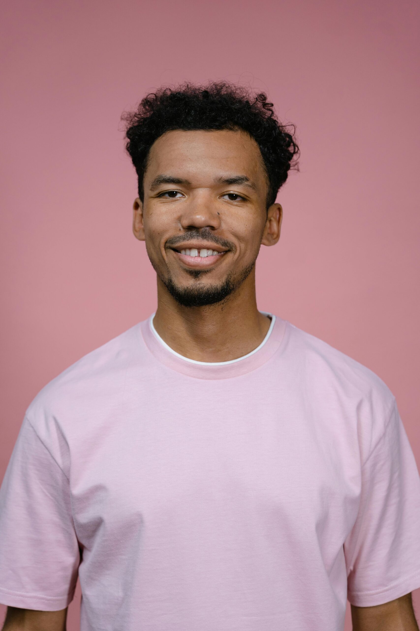 A cheerful man in a pink shirt smiling against a pink background in a studio.