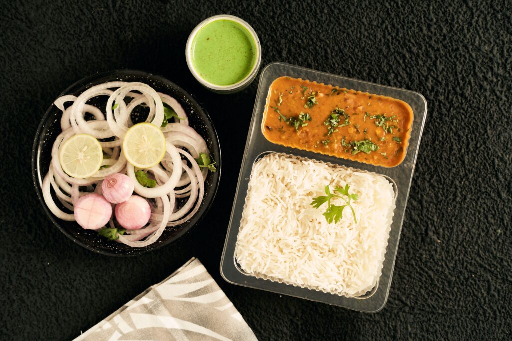 Delicious Indian meal featuring daal, white rice, onion salad, and green chutney from a top view perspective.